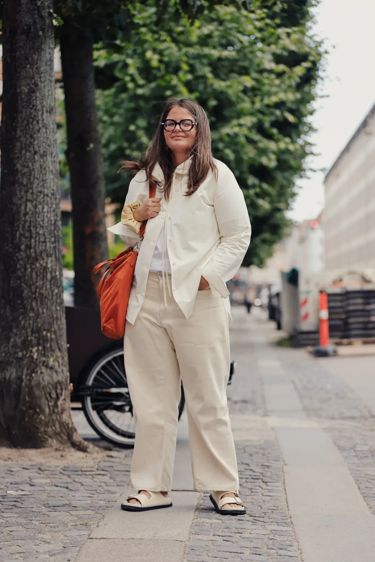 A Scandinavian woman in a white blazer and pants standing on a sidewalk.