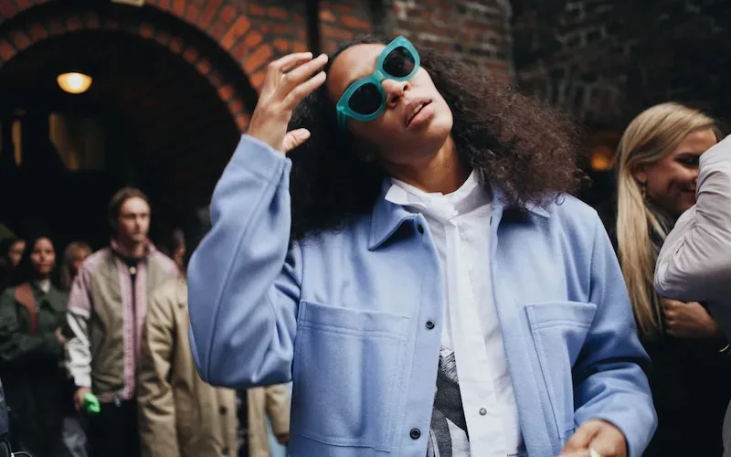 A woman wearing a blue jacket and sunglasses stands out in the crowd at events in Copenhagen.