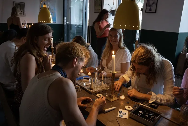 A group of people sitting at a table and making jewelry.